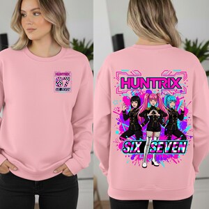 May include: Pink sweatshirt with the text "HUNTRIX" and "SIX SEVEN". The front features a small graphic with the text "HUNTRIX" and "67". The back has a larger graphic of three anime-style characters with colorful accents.