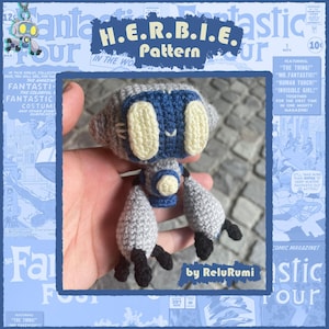 Puede incluir: Un juguete de robot de ganchillo hecho a mano en colores gris, azul y crema. El robot tiene ojos grandes y ovalados y una cara sonriente. El texto "H.E.R.B.I.E. Pattern" es visible en el fondo, junto con gráficos de estilo cómic.