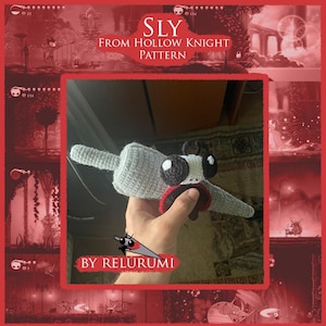 May include: Crocheted Sly toy from the Hollow Knight pattern. The plush has a grey body, large black and white eyes, and a red and black accent. The text "SLY FROM HOLLOW KNIGHT PATTERN" is visible in the background.