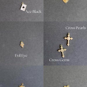 K&ouml;nnte beinhalten: Eine Sammlung goldfarbener Charms, darunter Ace Red und Ace Black Spielkarten, ein herzf&ouml;rmiges Fireheart, ein Evil Eye, Cross Pearls und Cross Gems Kreuze, eine Sonne und ein Liebesbrief. Jeder Charm hat eine kleine Schlaufe zur Befestigung.