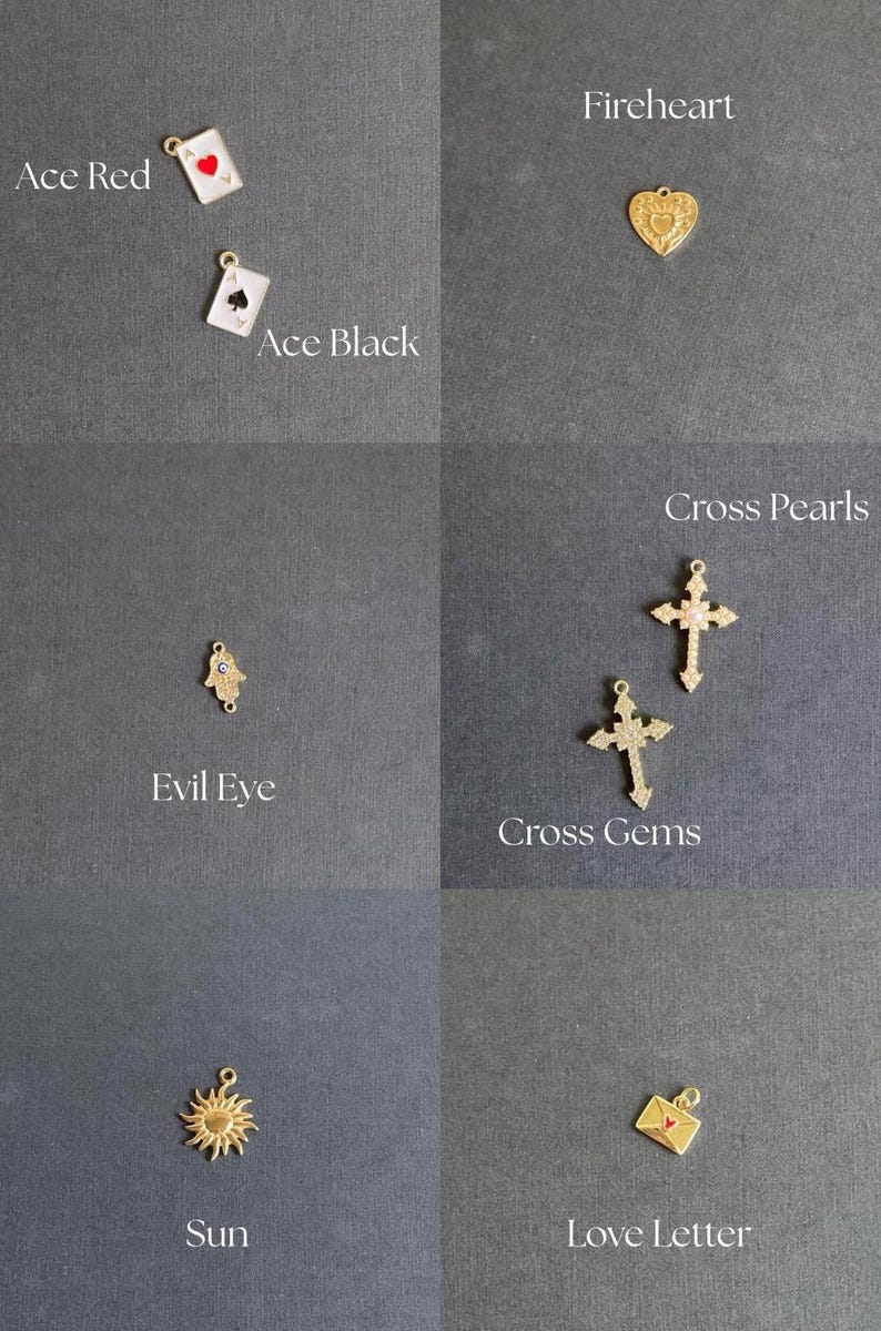 K&ouml;nnte beinhalten: Eine Sammlung goldfarbener Charms, darunter Ace Red und Ace Black Spielkarten, ein herzf&ouml;rmiges Fireheart, ein Evil Eye, Cross Pearls und Cross Gems Kreuze, eine Sonne und ein Liebesbrief. Jeder Charm hat eine kleine Schlaufe zur Befestigung.
