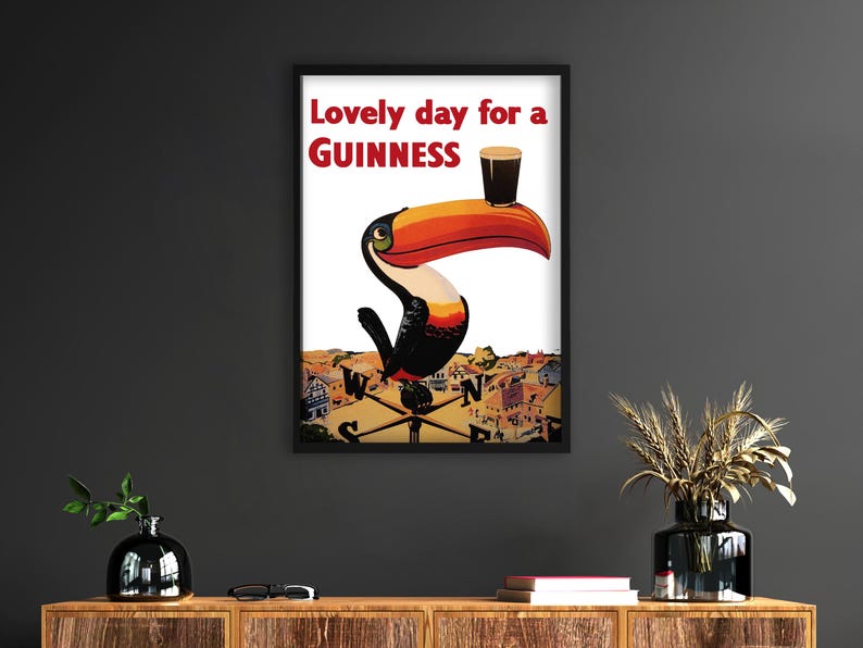 May include: Framed poster featuring a toucan with a Guinness pint balanced on its beak. The poster has the text "Lovely day for a Guinness" in red. The toucan is set against a backdrop of a town.