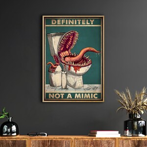 K&ouml;nnte beinhalten: Ein gerahmtes Poster mit dem Text "DEFINITELY NOT A MIMIC" zeigt eine Cartoon-Illustration eines Monsters, das aus einer Toilette auftaucht. Das Monster hat einen gro&szlig;en Mund mit scharfen Z&auml;hnen und einer langen Zunge, mit einem teal Hintergrund.