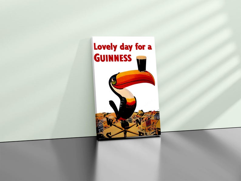 May include: A framed print featuring a toucan with a Guinness pint balanced on its beak. The artwork includes the text "Lovely day for a Guinness" in red. The background depicts a town with a compass.
