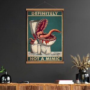 K&ouml;nnte beinhalten: Ein Poster mit dem Text "DEFINITELY NOT A MIMIC" zeigt eine Cartoon-Toilette mit einem monstr&ouml;sen Mund und einer Zunge. Das Kunstwerk ist vor einem teal-farbenen Hintergrund mit einem M&uuml;lleimer und einer Toilettenpapierrolle.