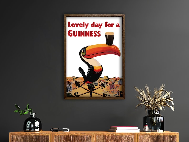 May include: Framed vintage Guinness advertisement featuring a toucan with a large orange and black beak, holding a pint of Guinness. The text reads "Lovely day for a Guinness" in red letters.