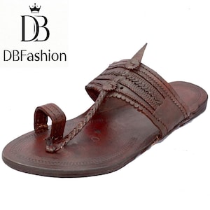 Könnte beinhalten: Braune Ledersandale mit Zehenschlaufe und Ziernähten. Die Sandale hat einen geflochtenen Riemen und ein strukturiertes Fußbett. Das Markenlogo "DBFashion" ist sichtbar.