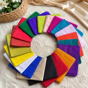 Peut inclure: Une collection d'échantillons de tissu rectangulaires disposés en cercle. Les échantillons présentent une grande variété de couleurs unies, notamment rouge, vert, bleu, jaune, blanc, noir, violet, rose, orange et beige avec une texture lisse.