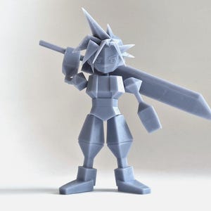 Puede incluir: Una figura gris claro de un personaje que sostiene una espada grande. La figura tiene el pelo puntiagudo y un diseño geométrico. La espada se sostiene sobre el hombro. La figura está sobre una superficie blanca.