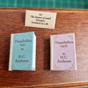 Puede incluir: Miniaturas de libros, "Thumbelina Vol I" en azul claro y "Thumbelina Vol II" en lavanda, de H.C. Andersen. Una pequeña tarjeta dice "To: The Keeper of small Wonders Verified by L.M."