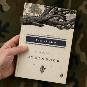 May include: A hardback book titled "East of Eden" by John Steinbeck. The cover features a black and white illustration of a tree and a horse. The book is a Steinbeck Centennial Edition.