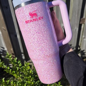 Peut inclure: Un gobelet Stanley rose paillet&eacute; avec une poign&eacute;e et un couvercle rose clair. Le logo Stanley est en rose. Le gobelet est tenu par une personne. Le texte "Sparkle Envy Creations" est en arri&egrave;re-plan.