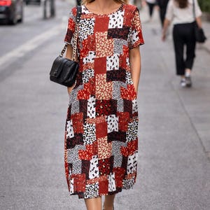 Könnte beinhalten: Midikleid mit Patchwork-Design in Rot, Schwarz, Weiß und Beige. Das Kleid hat kurze Ärmel und einen runden Ausschnitt. Eine schwarze Umhängetasche mit Kette und schwarze Sandalen vervollständigen den Look.