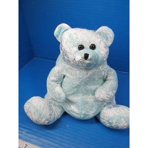 May include: A light blue plush teddy bear with black button eyes and a black nose. The bear has a soft, textured appearance and is sitting with its legs outstretched. The bear is a stuffed animal.
