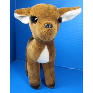 May include: A plush deer toy with brown fur, white patches, and large, expressive eyes. The deer has white-lined ears and a black nose. The toy is standing upright, showcasing its soft, cuddly appearance. A classic children's toy.