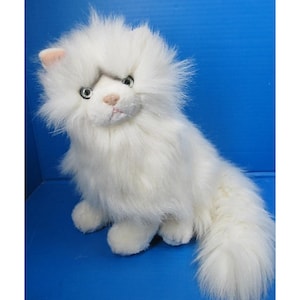 May include: A plush white cat with long, fluffy fur. The stuffed animal has a pink nose and ears, and green eyes. The cat is sitting upright with its tail curled to the side. The background is a solid blue.