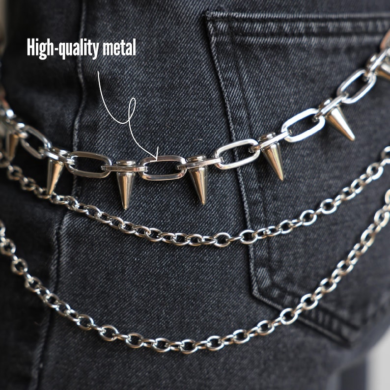 May include: Silver metal chain belt with three layers of chains and cone-shaped spikes. The text "High-quality metal" is visible in the image. The belt is worn over dark denim jeans.
