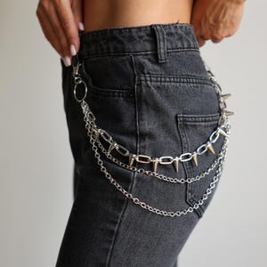 May include: Silver-toned chain belt with multiple layers and spiked accents. The belt features a lobster clasp and a mix of chain styles, adding a punk rock aesthetic to denim jeans. The belt is designed to be worn with jeans.