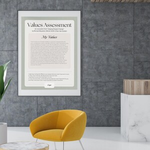 May include: A framed "Values Assessment" poster hangs on a gray wall. Below, a yellow armchair with silver legs sits near a round coffee table with a marble top and gold frame. A potted plant is on the left.