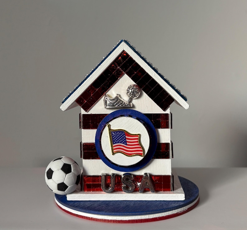 Handcrafted USA soccer themed miniature house with red white and blue mirrored accents, American flag emblem, and small soccer ball on base, shown on a clean neutral background