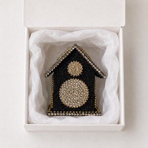 Black glitter and rhinestone keepsake house with gold accents nestled in white tissue paper inside an open gift box.