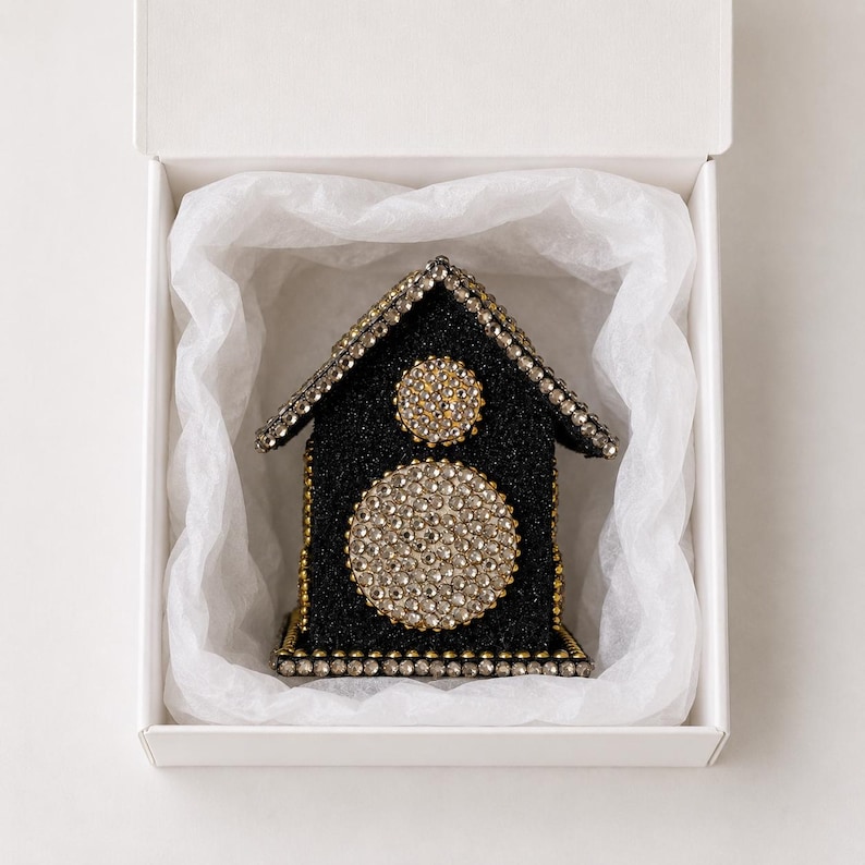 Black glitter and rhinestone keepsake house with gold accents nestled in white tissue paper inside an open gift box.