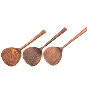 May include: Three wooden spatulas with long handles and wide, rounded heads. The spatulas are made of dark brown wood with visible grain patterns. The handles are smooth and tapered, and the heads are slightly curved.