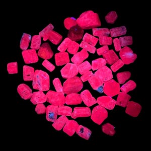 Pode incluir: Uma coleção de espécimes minerais rosa brilhantes e brilhantes contra um fundo preto. As pedras variam em tamanho e forma, com algumas mostrando toques de azul e roxo. O efeito geral é uma exibição vibrante e atraente de cristais naturais.