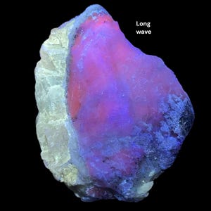 May include: A close-up of a rock formation with a vibrant display of colors. The rock has a white, rough exterior with a large section of pink and purple hues. The text "Long wave" is visible on the right side of the image.