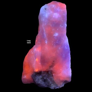 May include: A glowing, elongated mineral specimen with a dark base and a gradient of colors. The top is a soft purple, transitioning to pink and orange at the bottom. The text "Long wave" is visible.