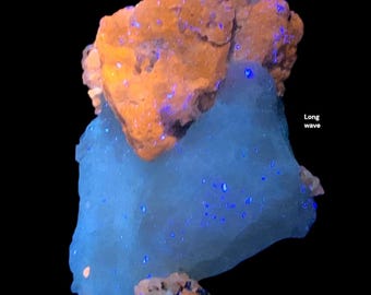 May include: A close-up of a mineral specimen with a dark background. The specimen has a large, light blue section with small, bright blue spots. An orange-brown section sits on top. The text "Long wave" is visible.