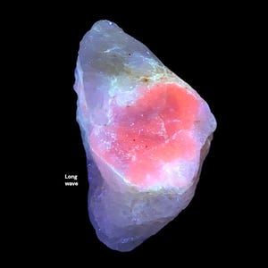 May include: A rough-cut, irregularly shaped mineral specimen with a vibrant pink center and a pale, translucent exterior. The text "Long wave" is visible on the left side of the image. The mineral glows with a soft, ethereal light against a black background.