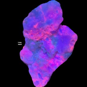 May include: A glowing, irregularly shaped rock formation with a black background. The rock displays a vibrant mix of colors, including shades of purple, pink, and blue. The text "Long wave" is visible in the image.