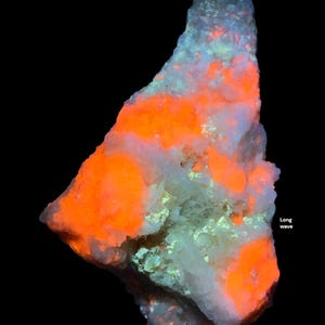 May include: A close-up of a mineral specimen with a black background. The mineral has a white base with patches of bright orange and areas of light blue and green. The text "Long wave" is visible on the right side.