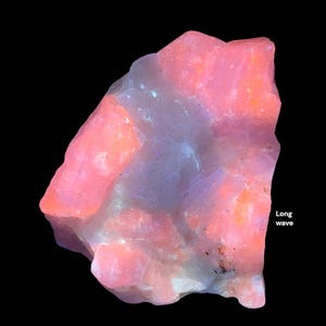 May include: A vibrant, irregularly shaped gemstone with a mix of pink, orange, and pale blue hues. The stone has a rough, textured surface and is set against a black background. The text "Long wave" is visible on the right side.