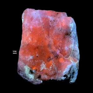May include: A close-up of a mineral specimen with a vibrant orange and pink hue, with areas of white and blue. The text "Long wave" is visible in the lower left corner. The background is black.