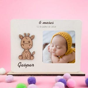 Pode incluir: Uma moldura retangular de madeira branca com uma figura de girafa em madeira cortada a laser à esquerda e uma foto de um bebé com um gorro de malha amarelo à direita. O texto 6 meses e 12 de Julho de 2024 aparece no topo, com o nome Gaspar.