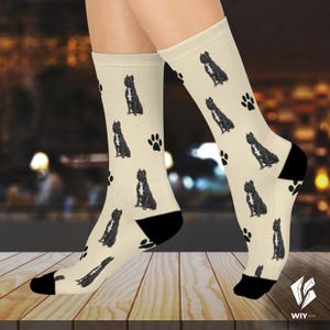 May include: Cream-colored socks featuring a repeating pattern of black dogs and paw prints. The socks have black heels and toes. The dog illustrations are detailed, and the paw prints are scattered across the fabric.