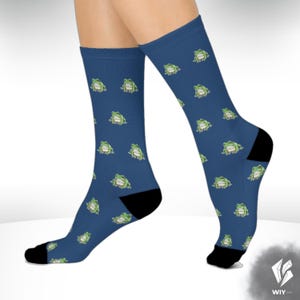 Könnte beinhalten: Blaue Socken mit einem sich wiederholenden Muster aus grünen Cartoon-Fröschen. Die Socken haben schwarze Fersen und Zehen. Die Socken sind kniehoch.