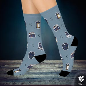 Peut inclure: Chaussettes bleu clair avec un motif répété d'appareils photo, de cartouches de film et d'objectifs. Les chaussettes ont des talons et des orteils noirs, avec de petits accents d'étoiles.
