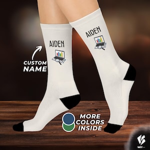 May include: A pair of white crew socks with black heels and toes. Each sock features the name AIDEN printed in black above a graphic of a laptop displaying a colorful bar chart, accompanied by a magnifying glass and a pen icon on the side.