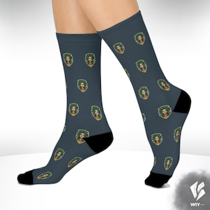 May include: A pair of dark teal socks with a repeating pattern of a woman's face with green hair and a gold-colored top. The socks have black heels and toes.