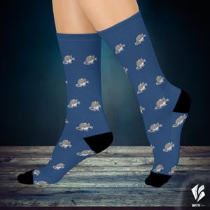 May include: A pair of crew-length socks in a deep blue colour featuring a repeating pattern of small, grey cartoon mice. The socks have solid black heels and toes, providing a distinct contrast to the blue fabric and the mouse illustrations.