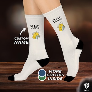 May include: A pair of white crew socks with black heels and toes. Each sock features the printed name ELIAS above a graphic of a yellow construction hard hat, a rolled blueprint, and a blue triangle ruler. The text CUSTOM NAME is visible.