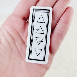May include: White sticker with a black border and four black geometric shapes inside. The shapes are a triangle, a triangle with a line through it, an upside down triangle, and a triangle with a line through it.