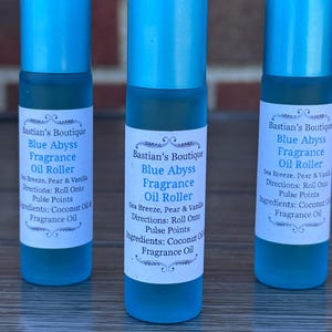 May include: Three blue fragrance oil rollers with white labels. The labels read "Bastian's Boutique Blue Abyss Fragrance Oil Roller" with directions and ingredients listed. The fragrance is described as Sea Breeze, Pear & Vanilla.