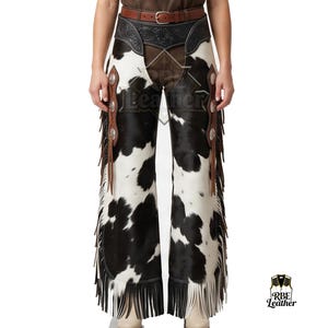 May include: Cowhide leather chaps featuring a black and white spotted pattern, a brown leather belt with a silver buckle, and brown leather side panels with silver conchos and long fringe. The lower edges are finished with black leather fringe.