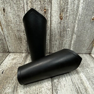 May include: Two black leather arm guards with a pointed top. The guards are made of thick leather and have a smooth finish.