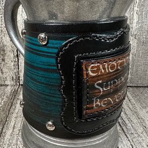 May include: A pewter tankard with a black leather wrap and a brown leather patch that says "Emotion Support Beverage".