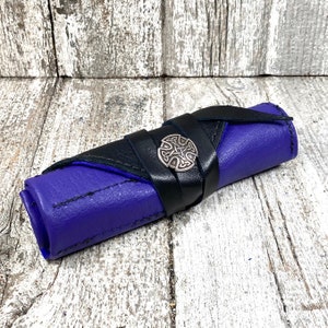 May include: A purple leather roll-up case with a black leather strap and a silver Celtic knot design. The case is rolled up and secured with the strap.